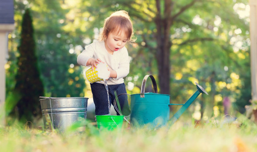 47987229 - happy toddler girl playing with watering cans outside